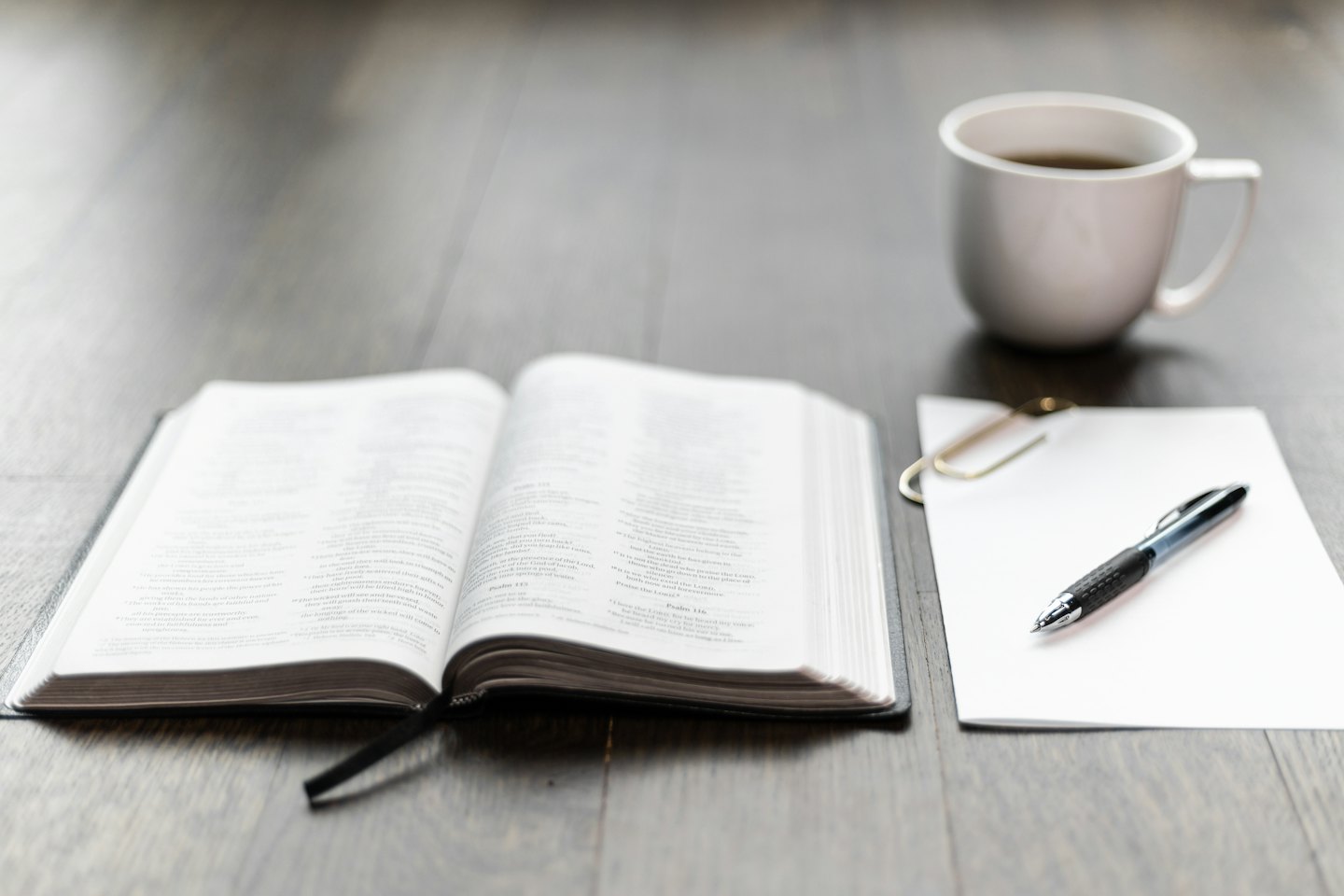 Libro aperto, foglio bianco, penna e caffè su una scrivania.