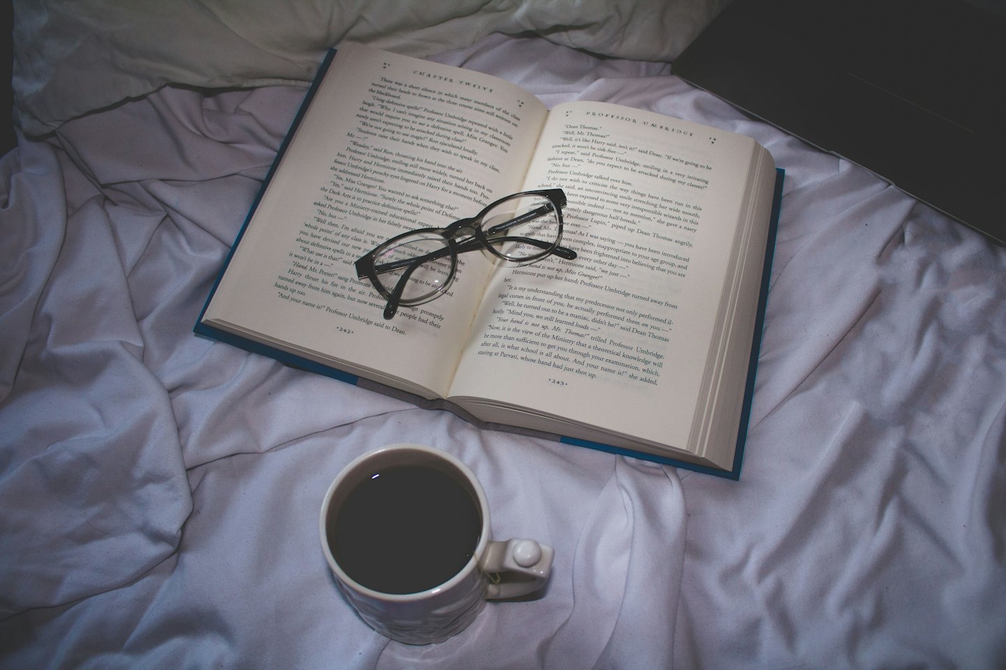 Libro aperto con occhiali da lettura e caffè su un letto.