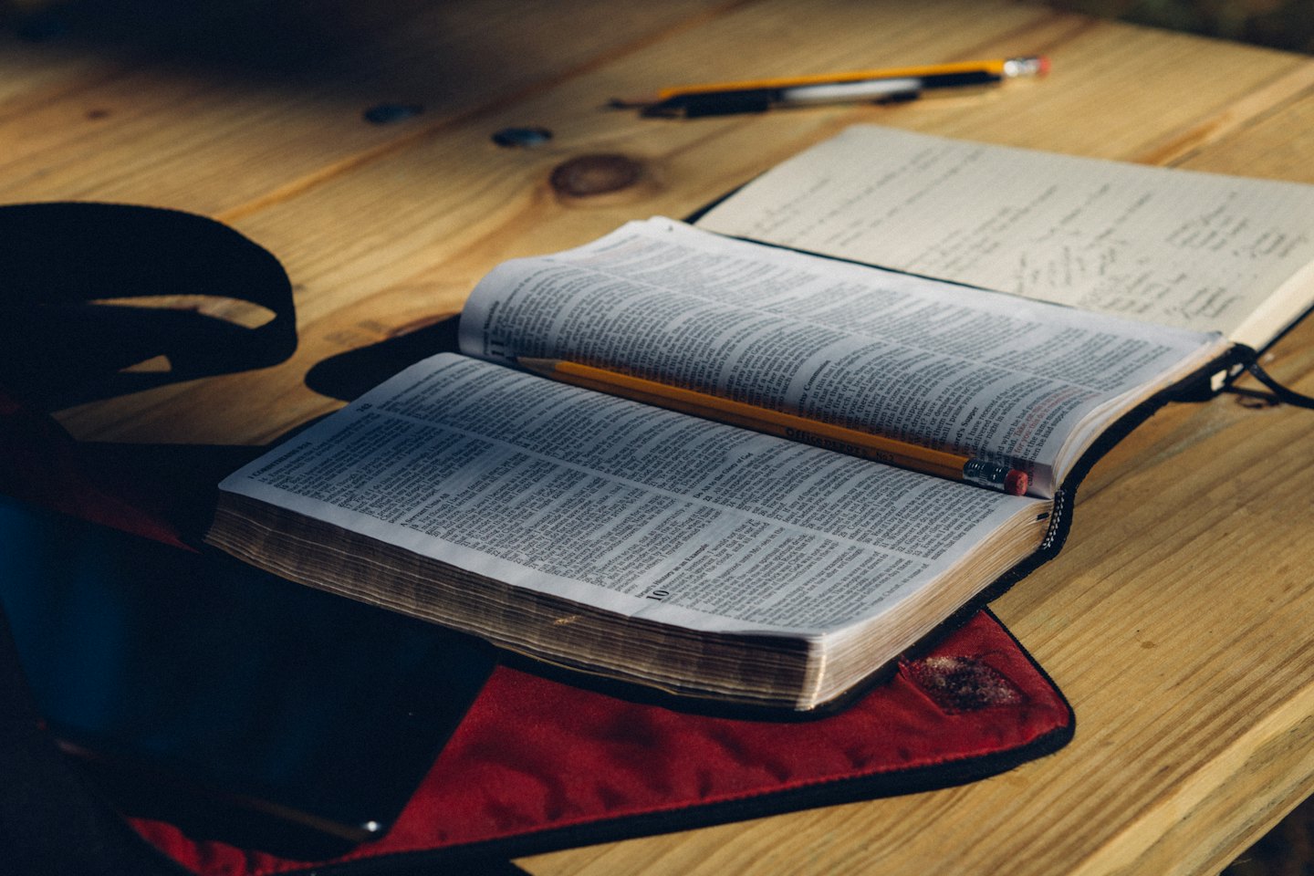 Bibbia aperta con matita e taccuino su tavolo di legno.